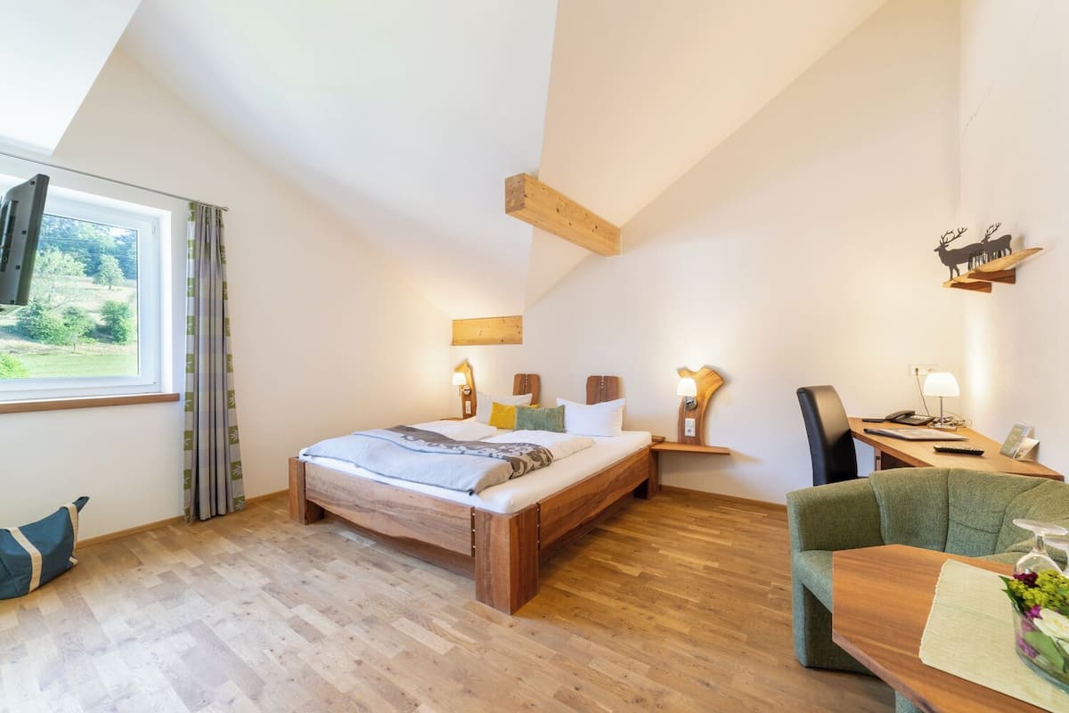 Ein Schlafzimmer mit einem hölzernen Bett, einem Schreibtisch mit Stuhl, einem Fenster mit Vorhängen und einem Wandregal mit einer Hirschdekoration.