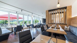 A modern restaurant with large windows, wooden tables, and black chairs. - Sontheims Naturhotel & Spa GmbH&Co.KG (Maierhöfen)