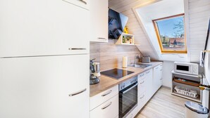 Uma cozinha moderna com armários brancos, forno embutido, micro-ondas e janela com vista para o exterior.
