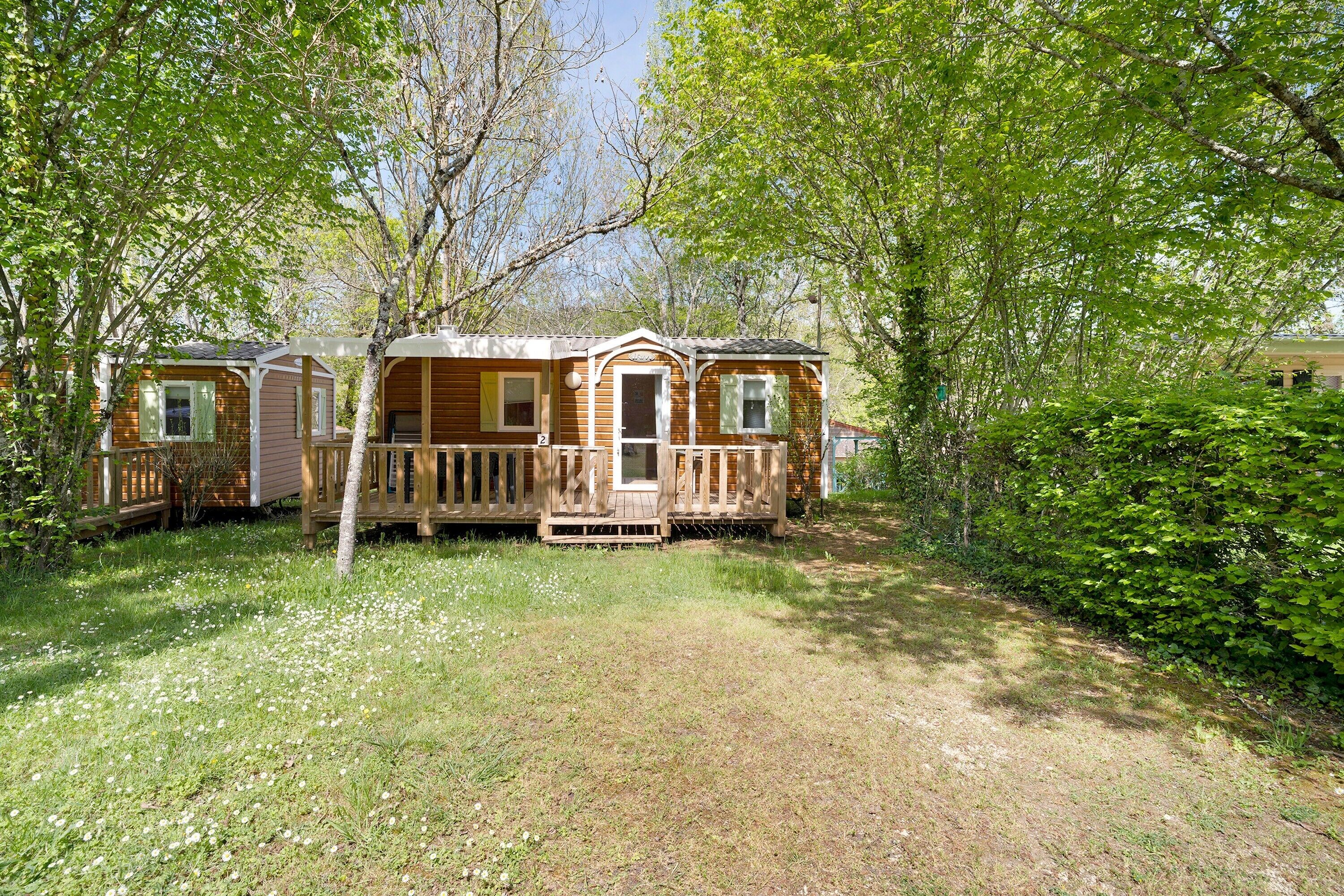 A mobile home with a deck, surrounded by trees and grass.