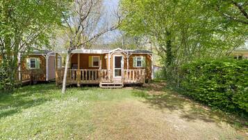 A mobile home with a deck, surrounded by trees and grass.