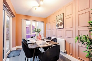 A dining area with a table set for four, a window with a view of a building, and a radiator on the wall.