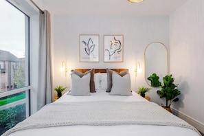 A hotel room with a large bed, two wall-mounted light fixtures, and two framed artworks. - 3BDR Terracotta House | Free Parking and Garden (Stoke-on-Trent)