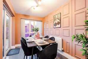 Un comedor con una mesa lista para cuatro, una ventana que da a un edificio y un radiador en la pared.