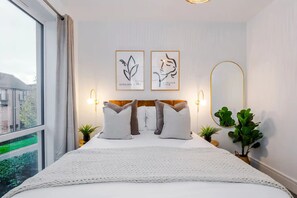 A hotel room with a large bed, two wall-mounted light fixtures, and two framed artworks. - 3BDR Terracotta House | Free Parking and Garden (Stoke-on-Trent)