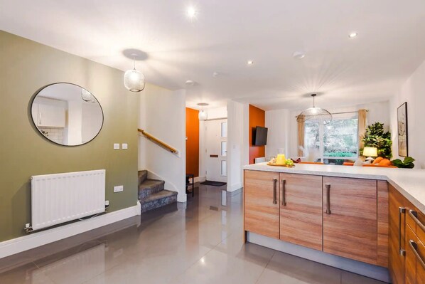 A modern kitchen with a central island, a staircase, and a view of the outdoors.