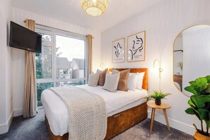 Habitación de hotel con cama, televisor, ventana con cortinas y una obra de arte en la pared.