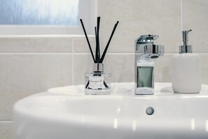 A bathroom sink with a clear glass bottle labeled 'Pomegranate' and a modern faucet. - 3BDR Terracotta House | Free Parking and Garden (Stoke-on-Trent)