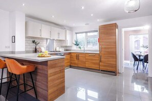 A modern kitchen with a central island, wooden cabinets, and a dining area with chairs. - 3BDR Terracotta House | Free Parking and Garden (Stoke-on-Trent)