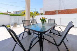 A patio with a glass table and chairs, a vase with flowers, and a white wall with a red brick section.