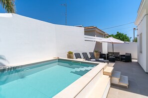 A swimming pool with steps leading into it, outdoor seating with umbrellas, and a white wall. - Villa 'Falaride' with Private Pool, Wi-Fi, and Air Conditioning (Avola)