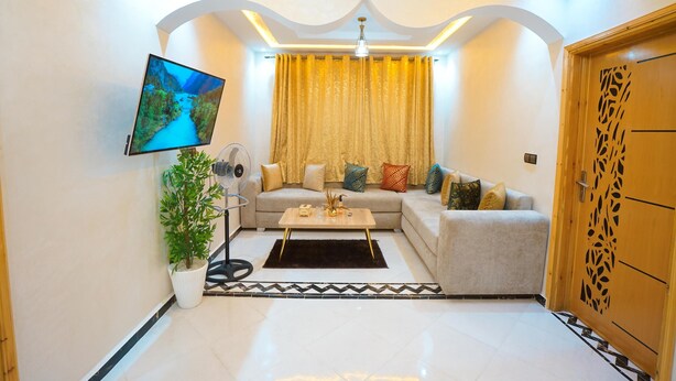 Una sala de estar moderna con un sofá, una mesa de centro, un televisor montado en la pared y una planta decorativa.