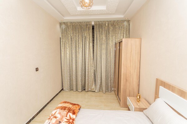 A bedroom with a bed, nightstand, wardrobe, and curtains.