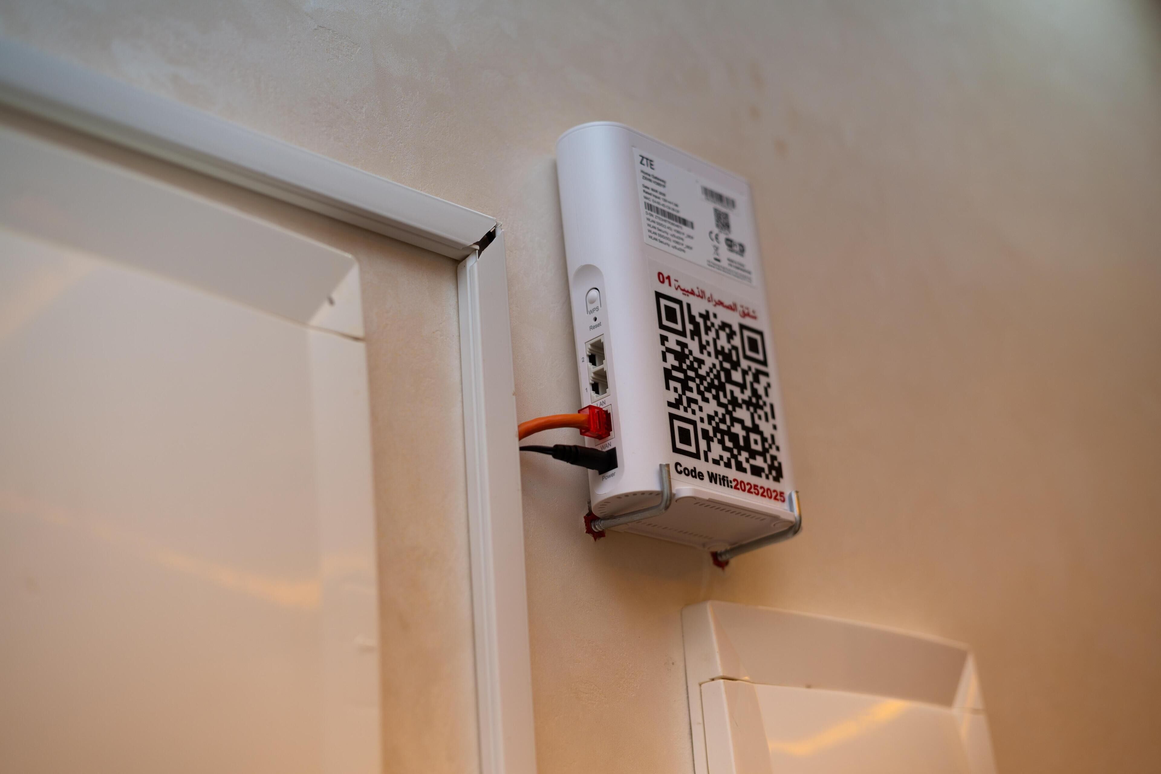 A QR code on a wall-mounted device, likely a Wi-Fi router, with visible cables and a door frame.