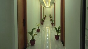 Un largo pasillo bien iluminado con puertas de madera a ambos lados, plantas en macetas a lo largo del centro y un piso reflectante.