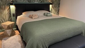 Un lit bien fait, recouvert d’une couverture verte, une table de chevet en bois et un banc.