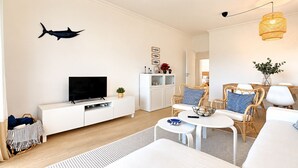 Uma sala de estar moderna com uma televisão de tela plana sobre um console branco, mobiliário de vime e um peixe decorativo na parede.