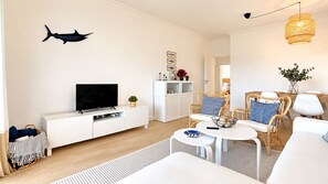 A modern living room with a flat-screen TV on a white console, wicker furniture, and a decorative fish on the wall. - Las Palmeiras Vilamoura (Vilamoura)
