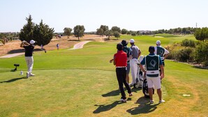 Um campo de golfe com um caminho bem definido, árvores e um grupo de pessoas em pé na relva.
