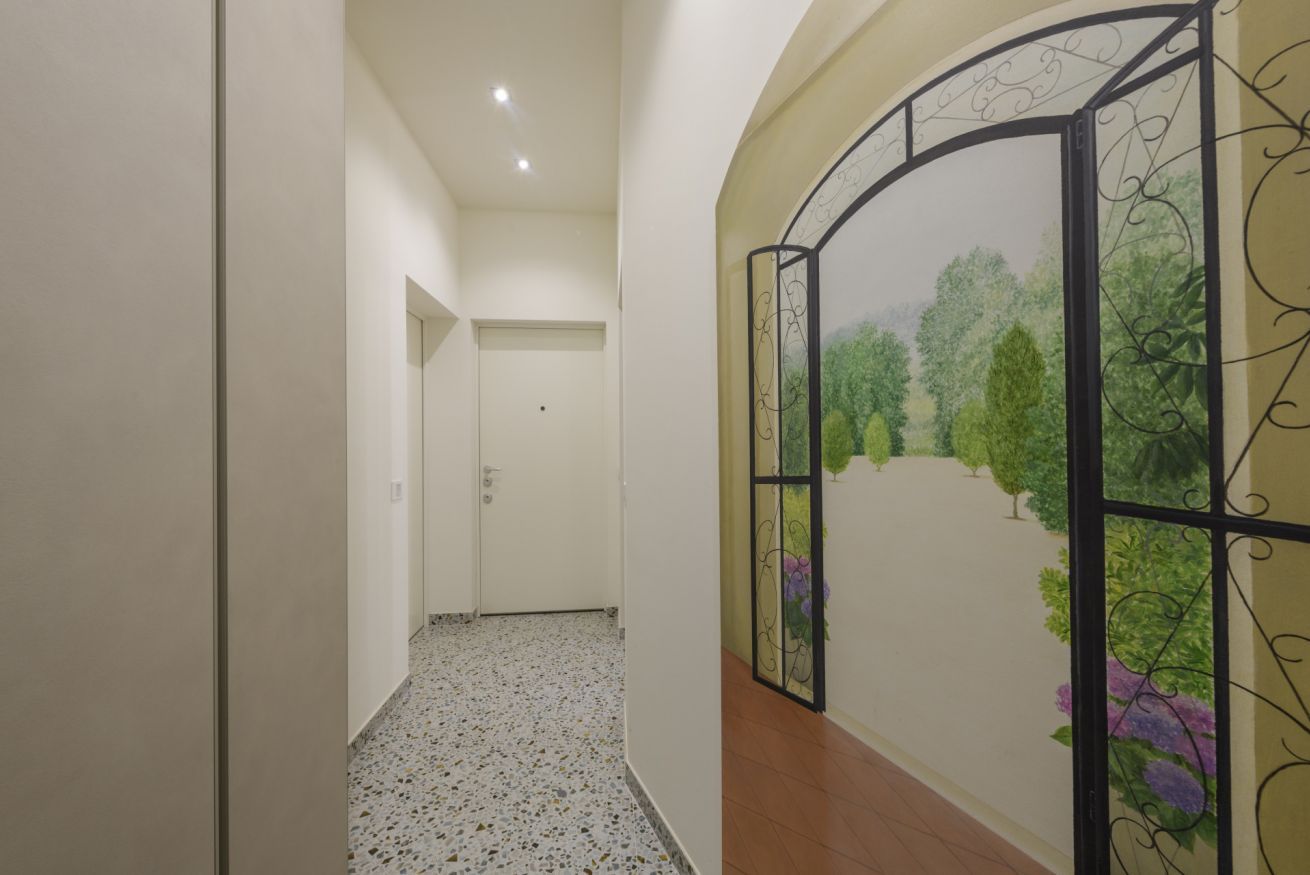 A hallway with a tiled floor, a white door at the end, and a decorative wall with a painted landscape.