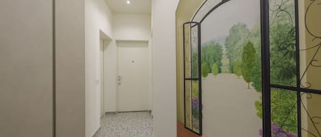 Un pasillo con suelo de baldosas, una puerta blanca al final y una pared decorativa con un paisaje pintado.