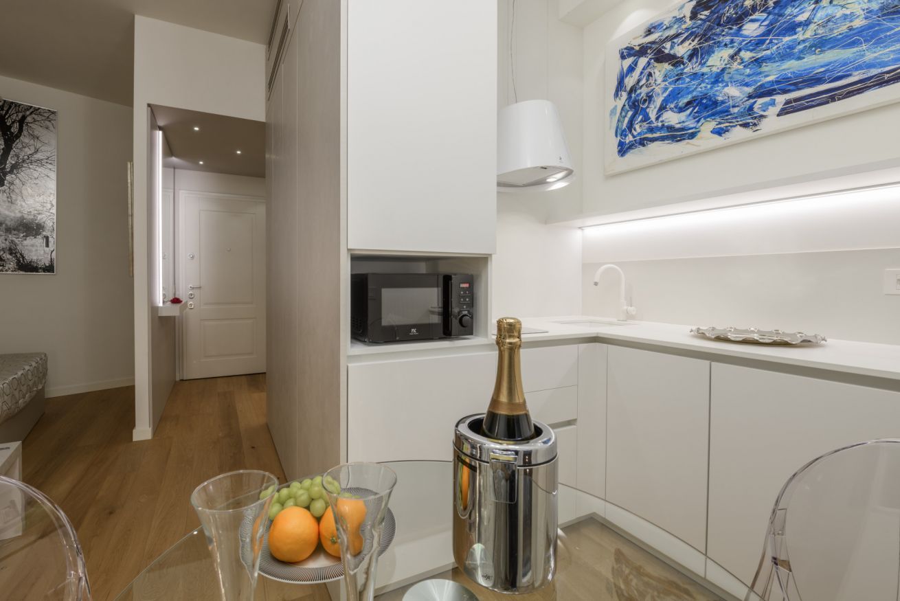 A modern kitchen with a microwave, a bottle of champagne, and a fruit bowl.