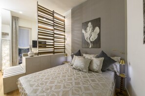 A bedroom with a bed, a window with blinds, a painting on the wall, and a bedside table with a lamp. - Gian Giacomo Mora, 13 - Refined studio apartment downtown (Milan)