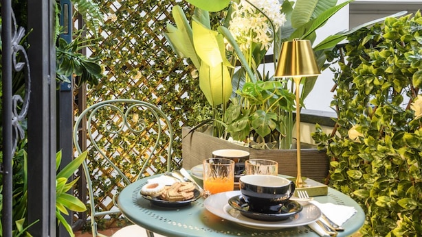 A table set with breakfast items, a lamp, and a chair in a lush, green outdoor area. - Gian Giacomo Mora, 13 - Refined studio apartment downtown (Milan)