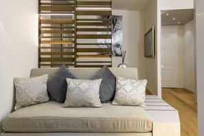 A modern living room with a sofa, patterned cushions, a decorative wall panel, and a framed picture. - Gian Giacomo Mora, 13 - Refined studio apartment downtown (Milan)