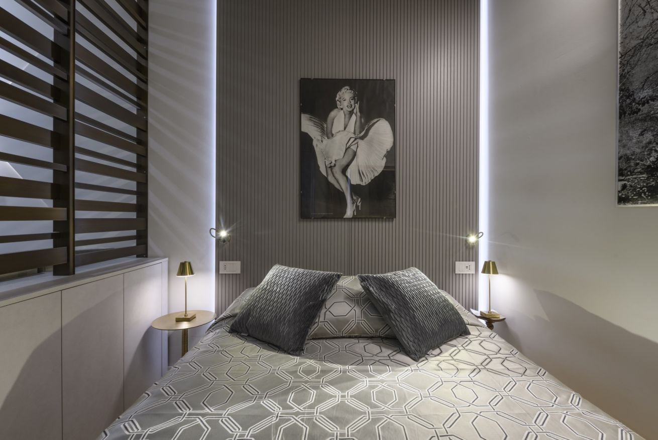 Um quarto moderno com colcha de padrão geométrico, uma obra de arte na parede e duas luminárias de cabeceira.