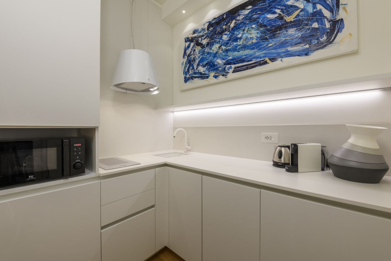 Una cocina moderna con armarios blancos, un microondas, una cafetera y un cuadro abstracto grande en la pared.