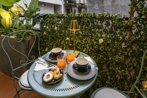 A table set with two cups, a glass of orange juice, and pastries, surrounded by greenery and a metal fence. - Gian Giacomo Mora, 13 - Elegant Studio Apartment in the City Center (Milan)