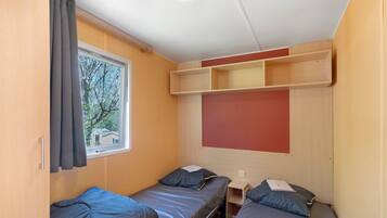 A small, compact room with two single beds, a window, and a built-in shelf above the beds.