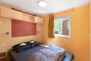 Une chambre à coucher comprenant un lit, une tête de lit, une fenêtre avec des rideaux et des étagères intégrées.