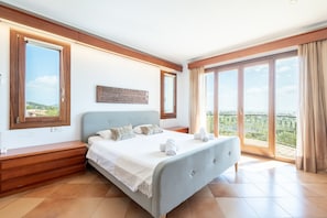 Ein Schlafzimmer mit Bett, Nachttischen aus Holz, einem großen Fenster und einem Balkon.