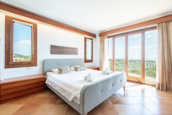 Une chambre à coucher avec un lit, des tables de chevet en bois, une grande fenêtre et un balcon.