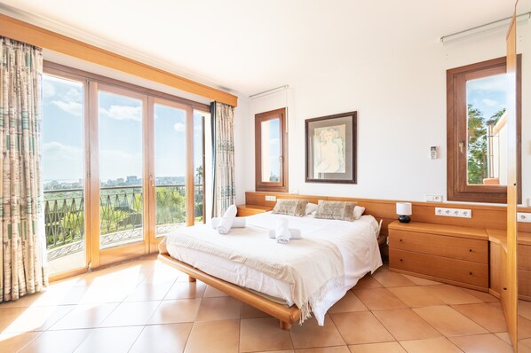 Ein Schlafzimmer mit einem großen Bett, einem Holz-Kopfteil, einem Nachttisch und Blick auf Grün durch große Fenster.