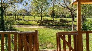 A wooden deck with a view of a grassy field and trees. - 3★ Campsite in Périgord Noir – Mobile Home with Pool, Fishing & Family Activities (Saint-Martial-de-Nabirat)