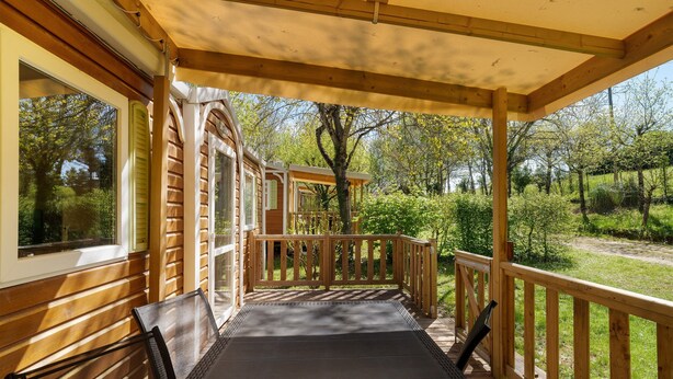 A covered outdoor area with wooden railings, a bench, and a view of a garden. - 3★ Campsite in Périgord Noir – Mobile Home with Pool, Fishing & Family Activities (Saint-Martial-de-Nabirat)