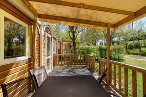 Un espacio al aire libre cubierto con barandillas de madera, un banco y vistas a un jardín.