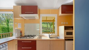 A compact kitchen with a gas stove, sink, and a microwave. - 3★ Campsite in Périgord Noir – Mobile Home with Pool, Fishing & Family Activities (Saint-Martial-de-Nabirat)