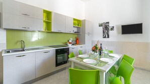 A modern kitchen with a dining area, including a TV, green chairs, and a table set for two. - Holiday Home 'Villa Anny Seafront' with Wi-Fi and Air Conditioning (Avola)