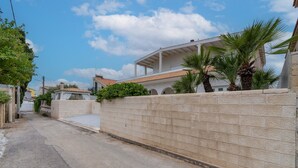 A narrow street with a stone wall, a building with a tiled roof, and a palm tree. - Holiday Home 'Villa Anny Seafront' with Wi-Fi and Air Conditioning (Avola)