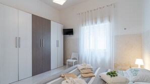 A modern bedroom with a bed, a TV, a chair, and a wardrobe. - Holiday Home 'Villa Anny Seafront' with Wi-Fi and Air Conditioning (Avola)