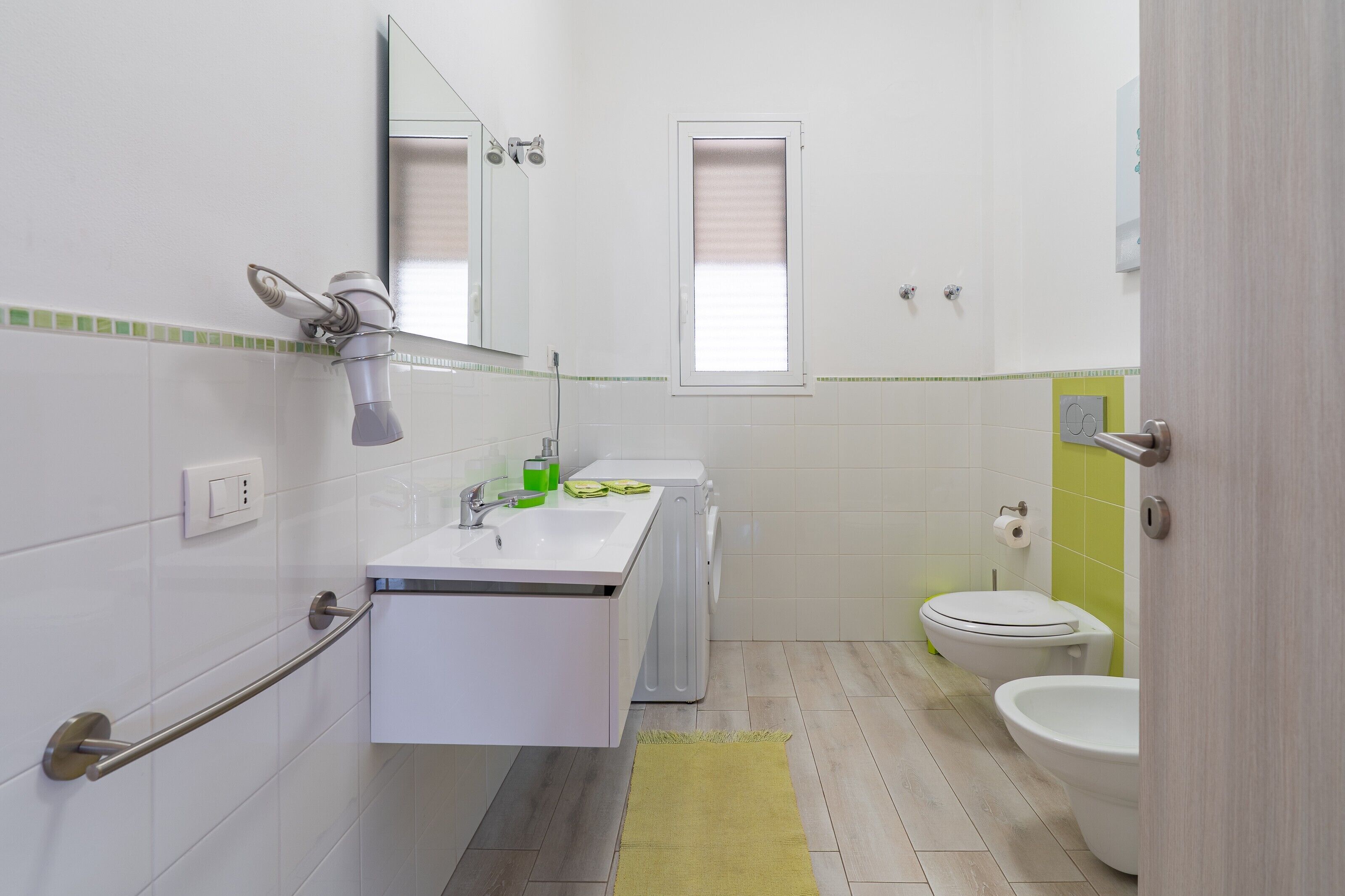 A bathroom with a sink, mirror, towel rack, toilet, and a window.