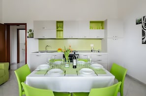Een moderne keuken met witte kasten, een eethoek met een tafel voor vier personen, en een groene accentmuur.