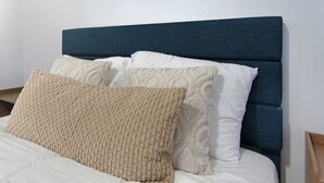 A bed with a dark headboard, white and beige pillows, and a white bedspread. - Cozy 2BR Apartment in Jersey City With Smart Lock (Jersey City)