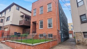 A two-story brick building with a small front yard and a black metal fence. - Cozy 2BR Apartment in Jersey City With Smart Lock (Jersey City)