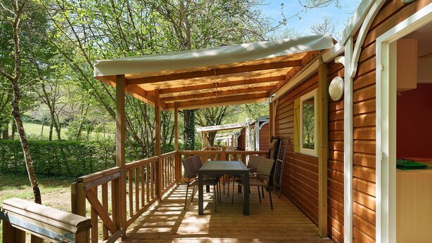 Une terrasse en bois dotée d’un espace salon couvert, d’une rambarde et offrant une vue sur la forêt environnante.