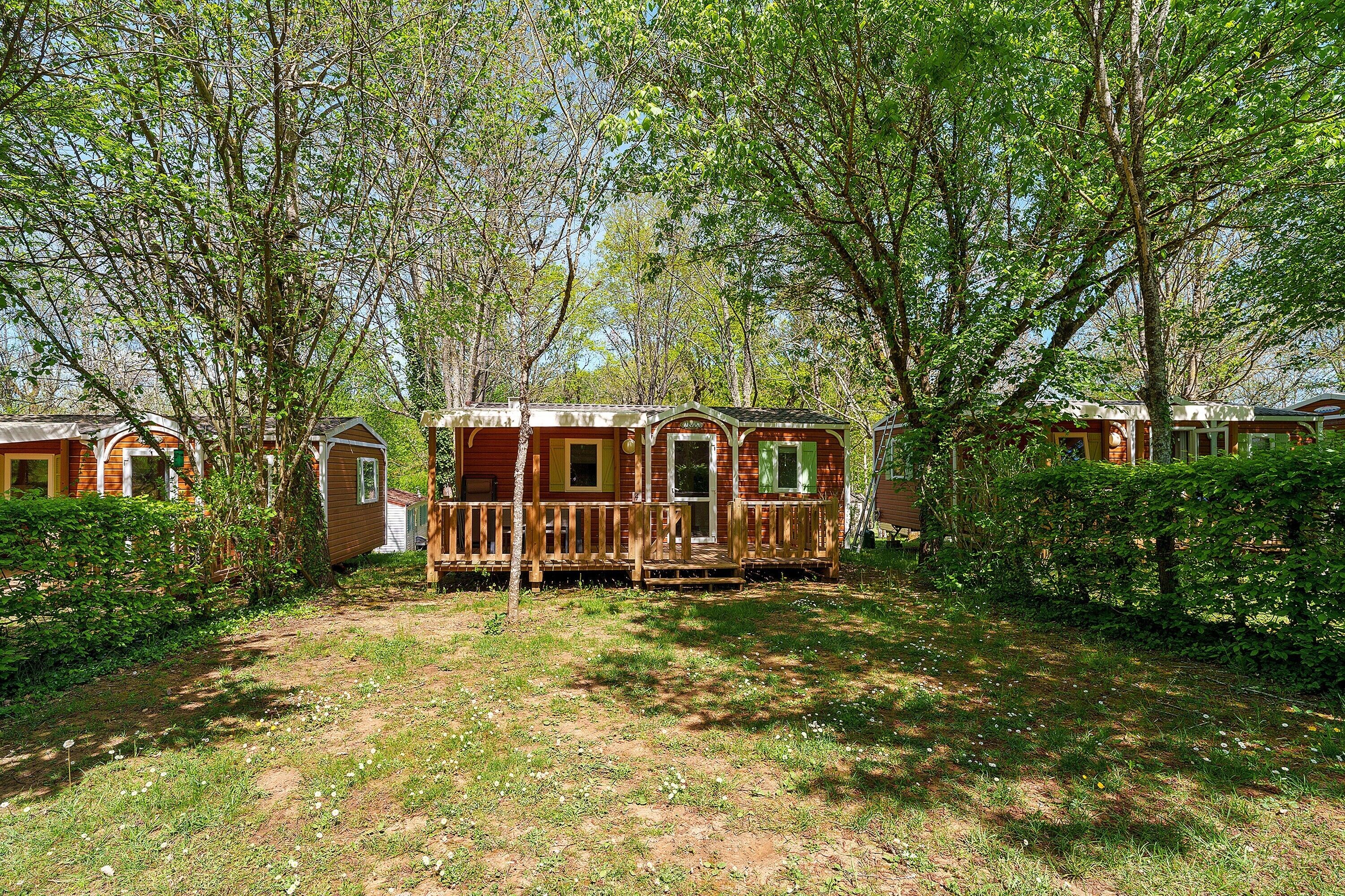 A wooden cabin with a porch, surrounded by trees and a grassy area.